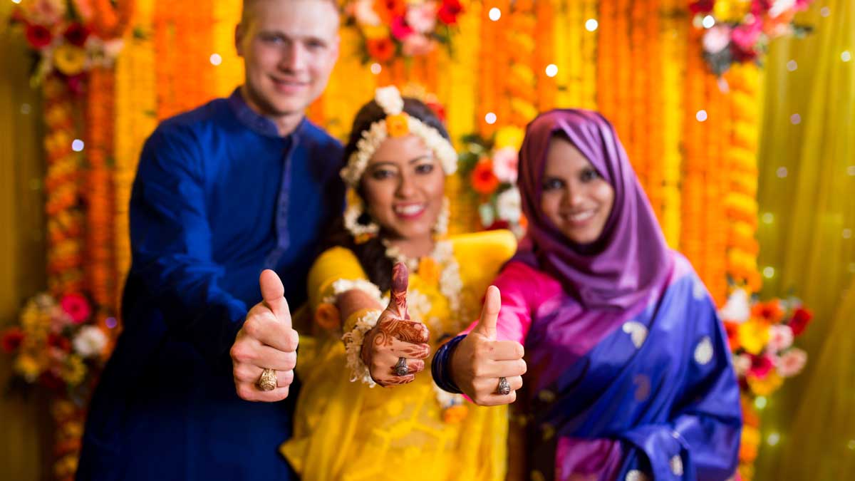 Three hands, one covered in henna tattoos, giving a thumbs-up and showing off their Aggie Rings